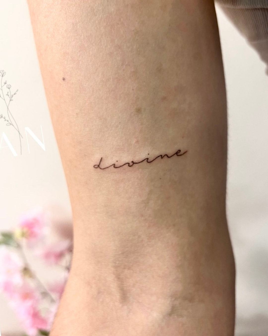 Fine line script 'divine' on arm